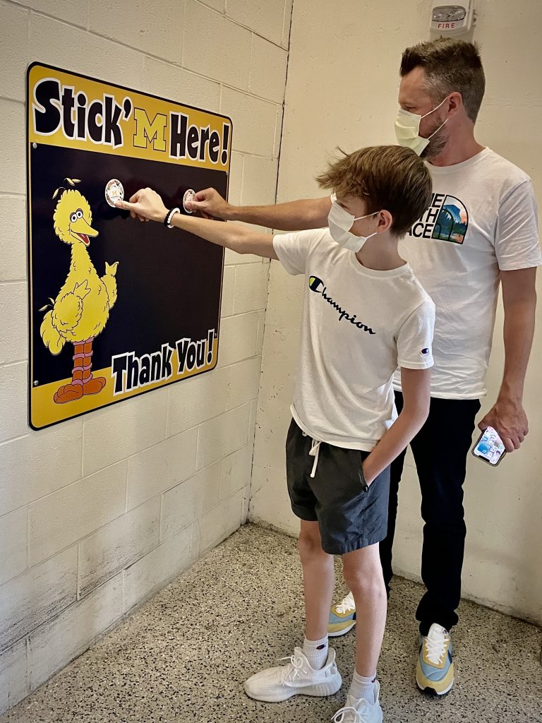 A dad and his son place their stickers on the Stick' M Here board in the parking structure after a visit.