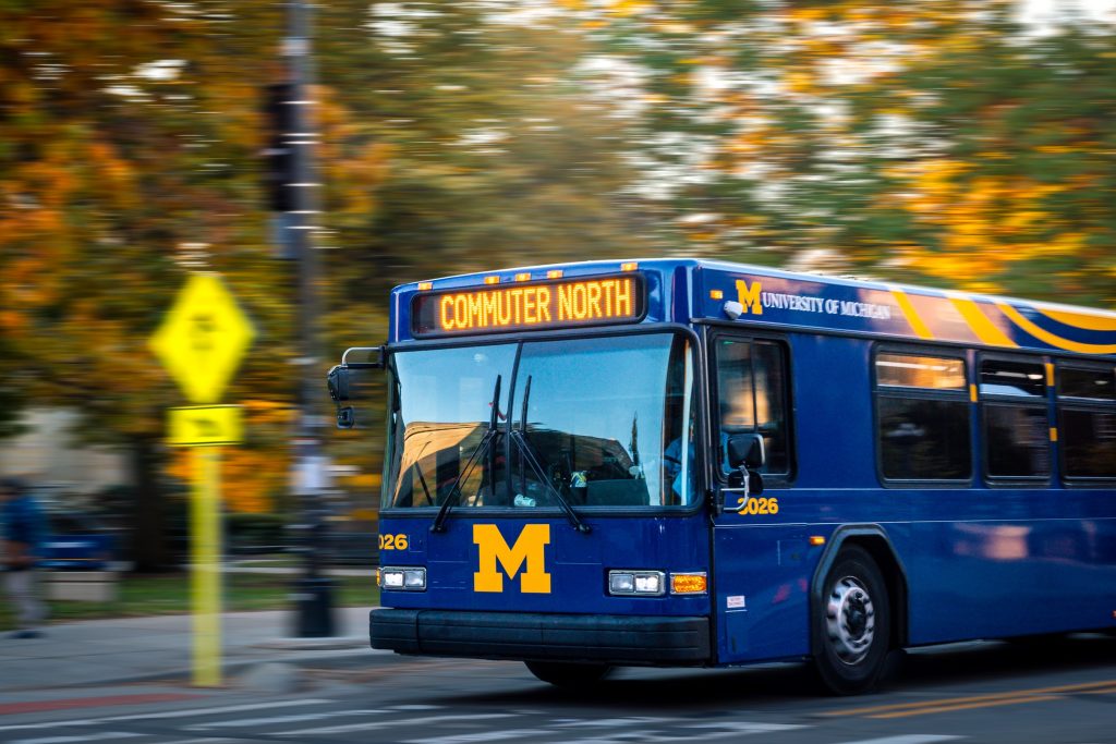 A blue bus drives past fall trees on campus.