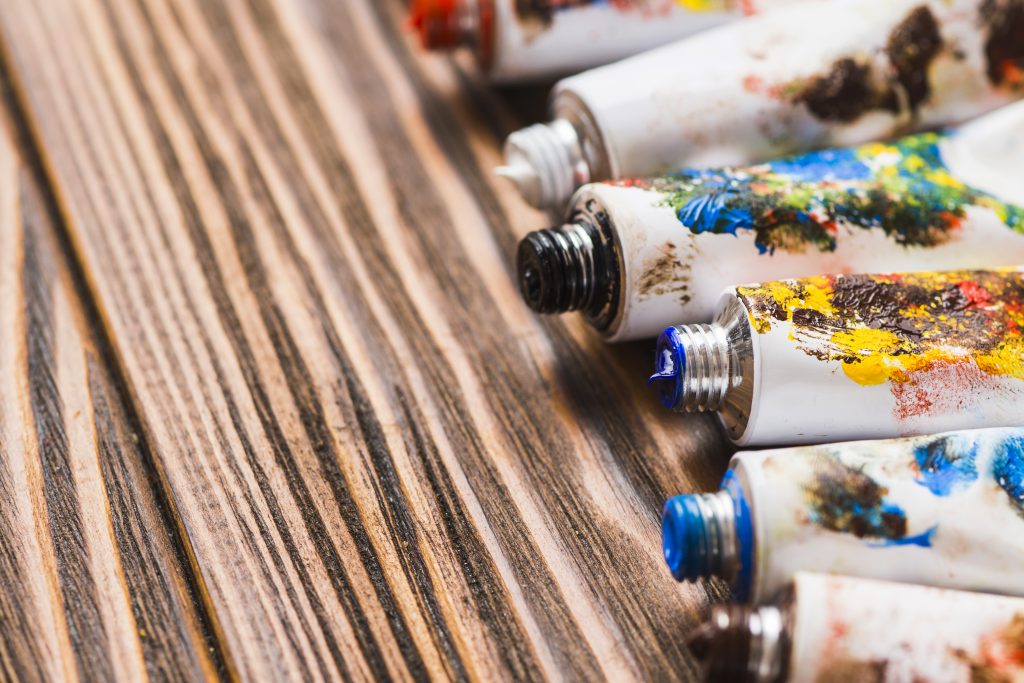 Tubes of used oil paint sit on a wooden table.
